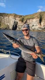 Angler proudly displaying a Barracuda while fishing near rocky coastal cliffs.