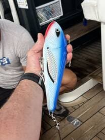 A close-up of a fishing lure being held on a boat, showcasing its vibrant blue and red colors.