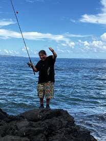 A young angler proudly displaying a small catch while fishing from rocky shores, with a stunning ocean backdrop.