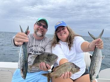 Two anglers proudly displaying their catch, including a large Spanish Mackerel and a Snapper, while enjoying a day on the water.