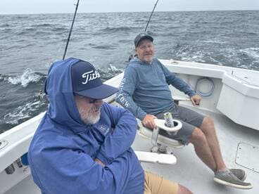 Two anglers relaxing on the boat, enjoying the ocean view while waiting for the next catch during a fishing trip.