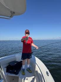A young angler proudly displaying a caught fish while fishing from a boat in calm waters.