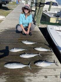 A woman poses beside a display of multiple Bonito fish laid out on a dock after a successful fishing trip.