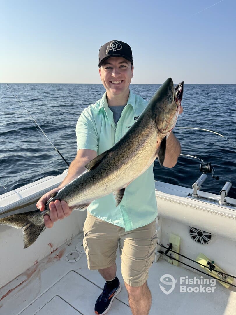 An angler proudly displaying a large Lake Trout while fishing on a boat in open waters.