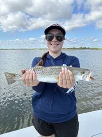 Angler proudly displaying a Speckled Trout while fishing on a calm waterway, showcasing a successful day on the water.