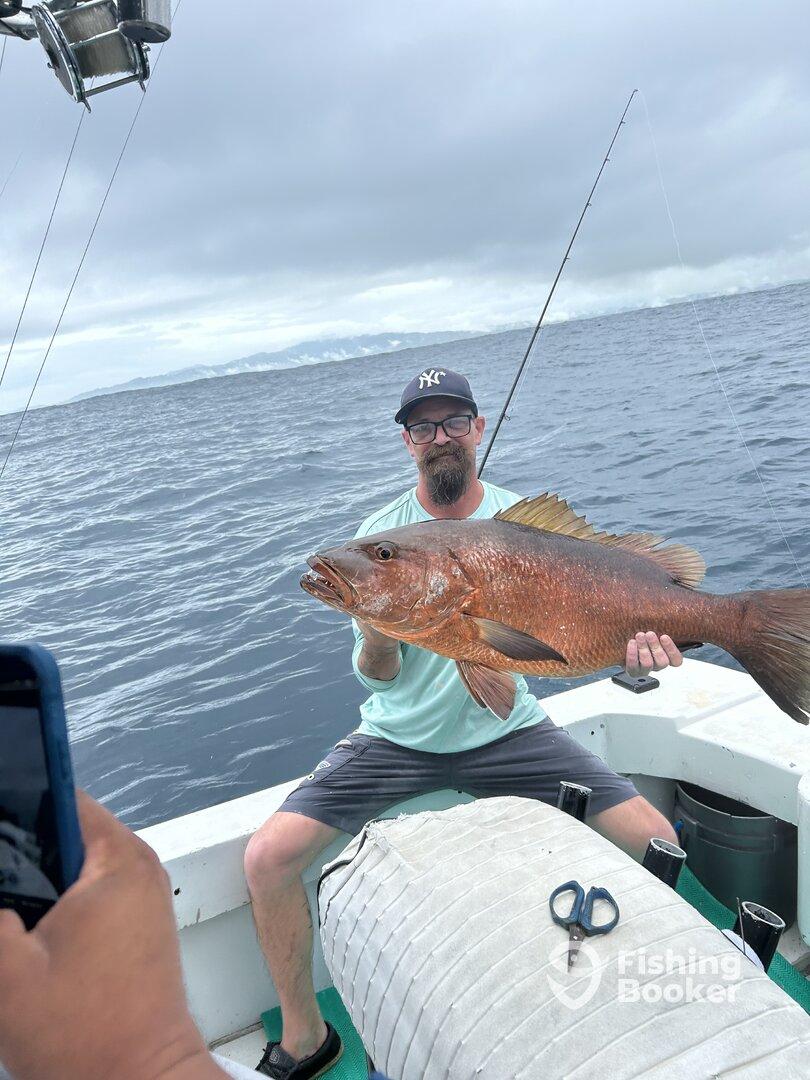 An angler proudly displaying a large Red Snapper while fishing on a boat in open waters.