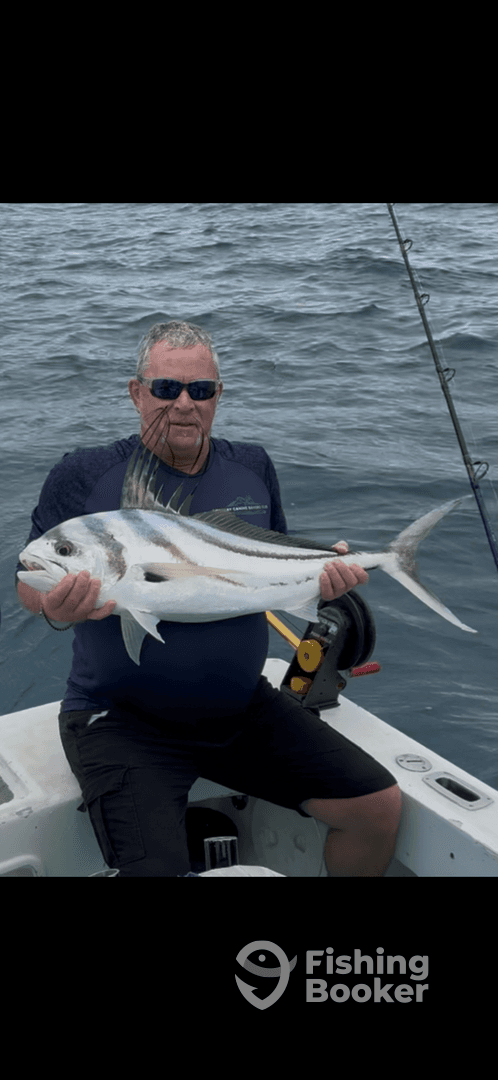 An angler proudly displaying a large Roosterfish while fishing from a small boat in open waters.