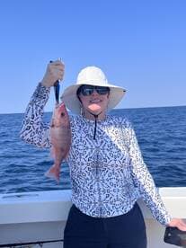 An angler proudly displaying a freshly caught Snapper while fishing offshore, showcasing a sunny day on the water.