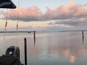 A serene view of a fishing boat at sunset, showcasing the calm waters and beautiful cloud reflections in the background.