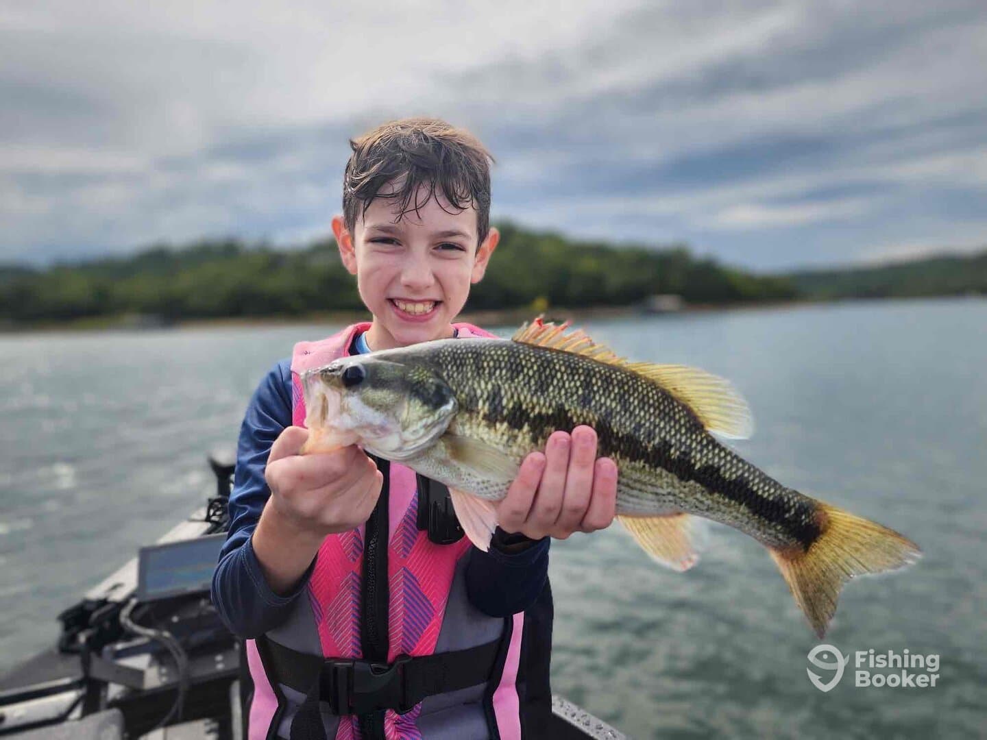 A young angler proudly displaying a large Largemouth Bass while fishing on a calm lake, showcasing a vibrant fishing environment.