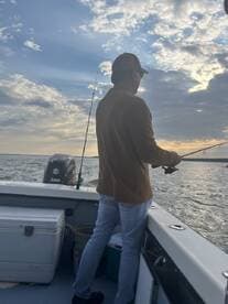 An angler casting a line while fishing on a boat during a scenic sunset, showcasing a tranquil fishing environment.