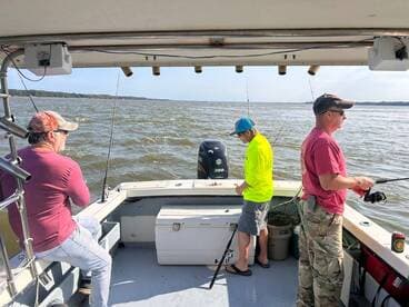 Three anglers actively fishing on a boat in a calm waterway, showcasing a relaxed fishing environment.