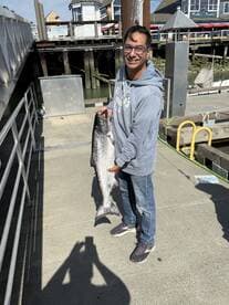 Angler proudly displaying a large Salmon at the dock, showcasing a successful fishing trip.