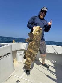 Angler displaying a large Goliath Grouper on a fishing charter in open waters, showcasing a successful catch.