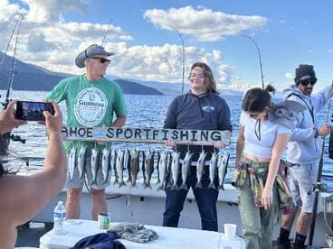 Group of anglers displaying their catch of trout on a board while enjoying a fishing trip on Lake Tahoe.