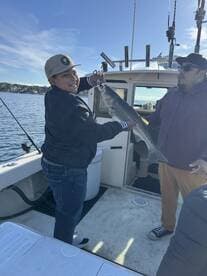 A young angler proudly displaying a striped bass aboard a fishing boat, enjoying a day on the water.