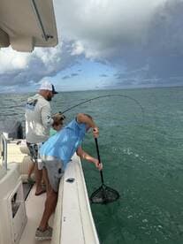 Two anglers actively fishing from a boat, with one preparing to net a catch in clear waters, showcasing a family-friendly fishing experience.