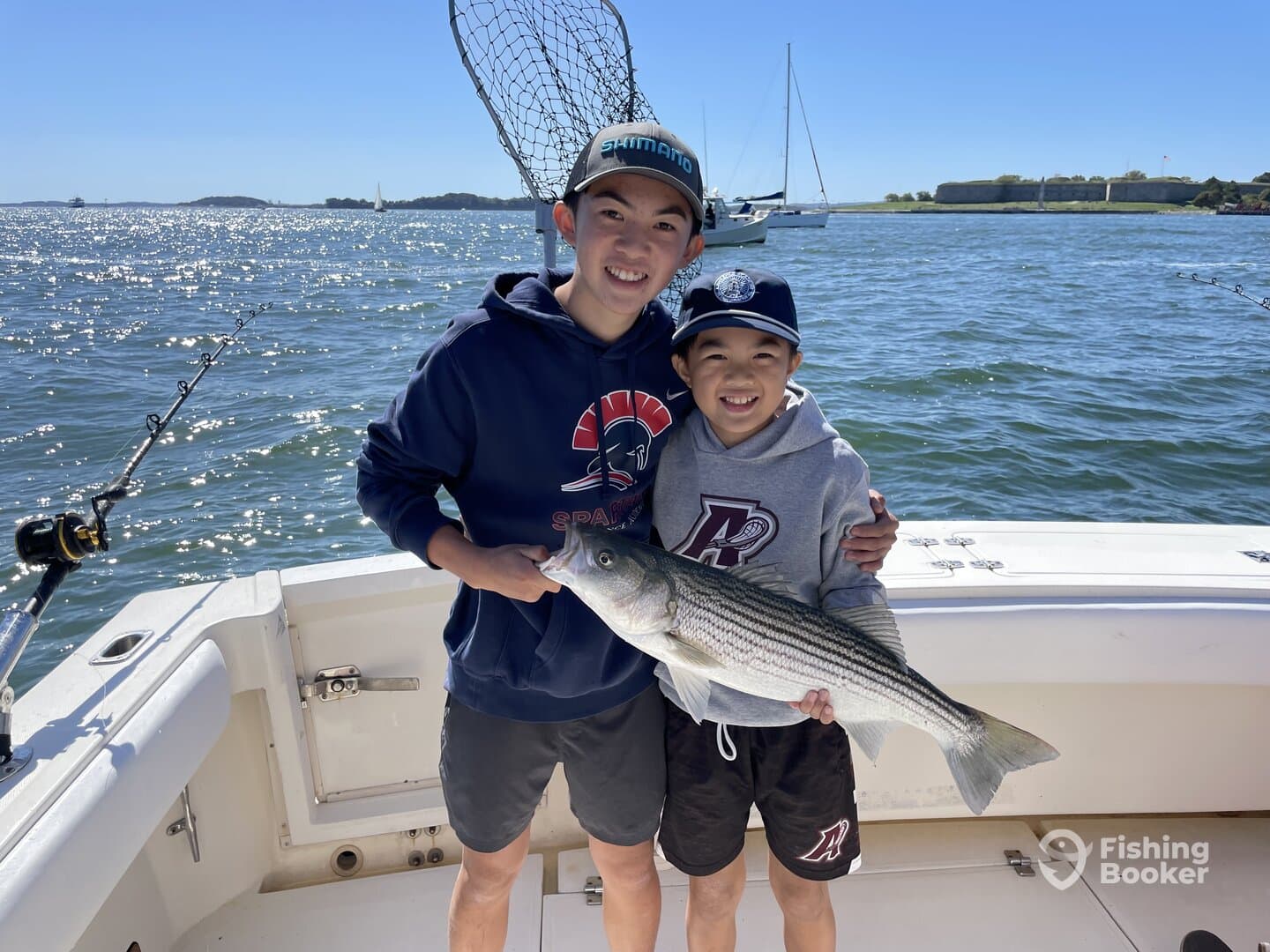 Two young anglers proudly displaying a large Striped Bass while fishing on a sunny day.