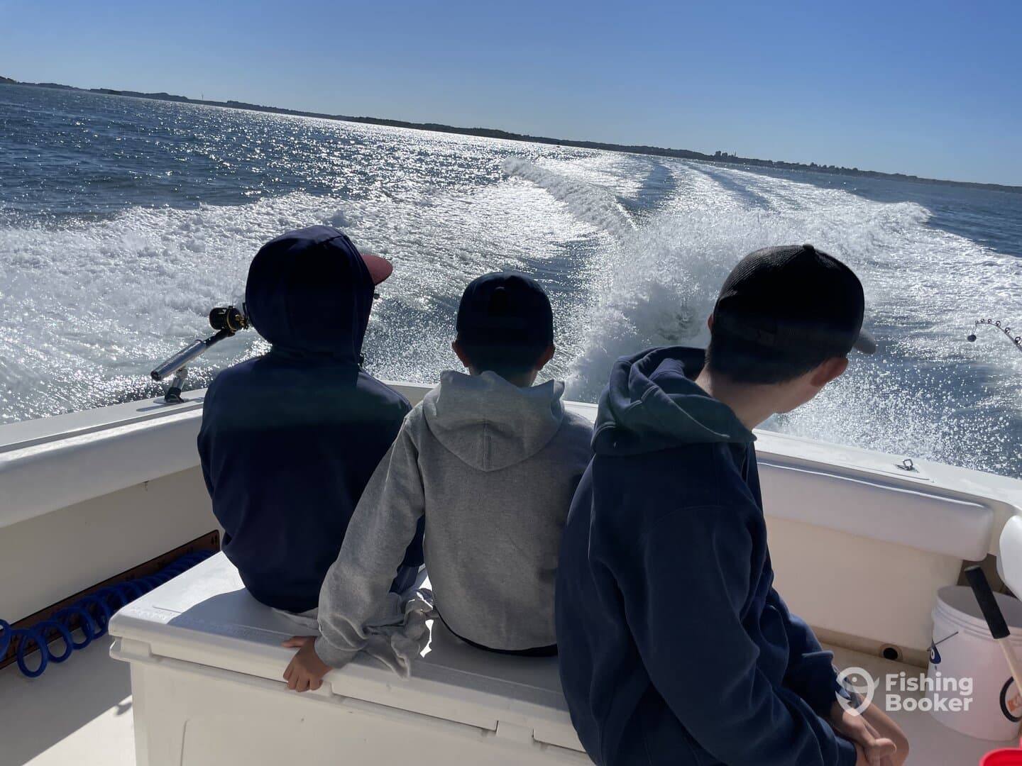 Three young anglers enjoying a boat ride, looking out over the sparkling water on a sunny day.