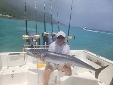An angler proudly displaying a large Wahoo while aboard a fishing boat in clear turquoise waters.