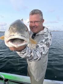 An angler proudly displaying a large Redfish while fishing on a calm waterway.