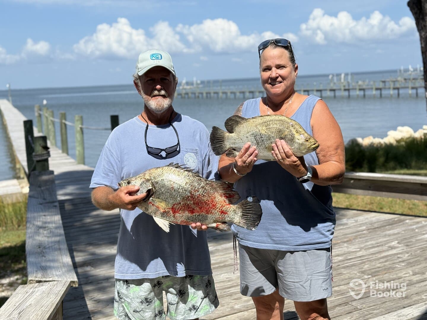 Two anglers proudly displaying their catch of large Tilapia on a sunny day at the dock.