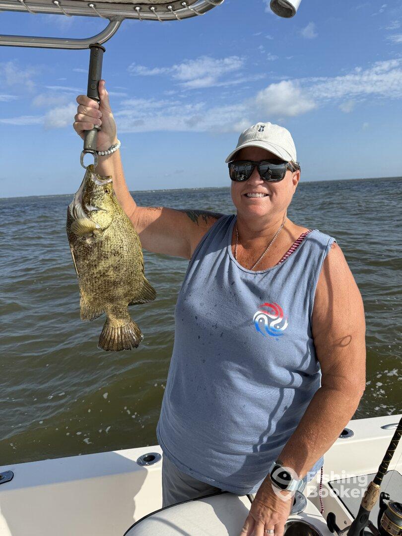 An angler proudly displaying a large Grouper while fishing on a boat, showcasing a successful day on the water.