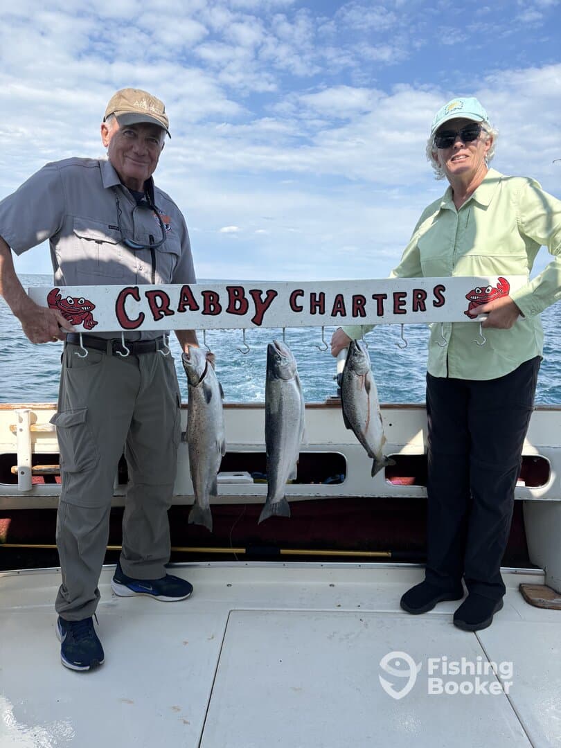 Two anglers proudly displaying their catch of fish while holding a sign for Crabby Charters on a fishing trip.