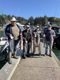 Four adult anglers proudly displaying their catch of Salmon at the dock after a successful fishing trip.