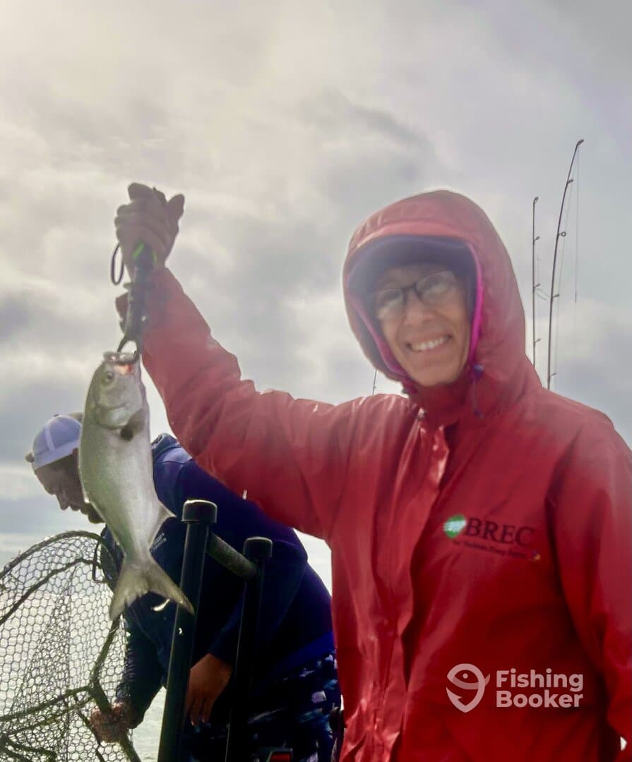 An angler proudly displaying a caught fish while fishing on a boat, showcasing a cloudy day on the water.