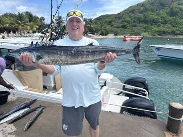 An angler proudly displaying a large Barracuda at the dock after a fishing trip in a tropical setting.