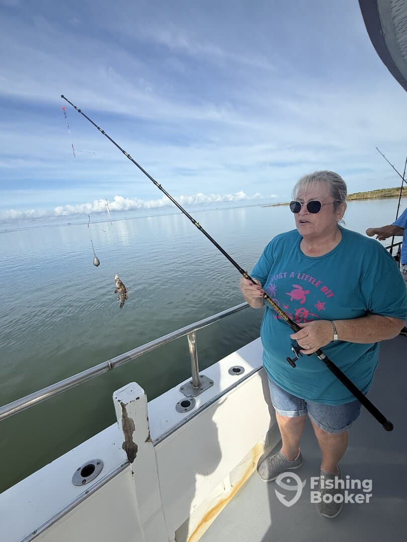 An angler reeling in a fish while fishing from a boat in calm waters, showcasing a relaxed fishing environment.