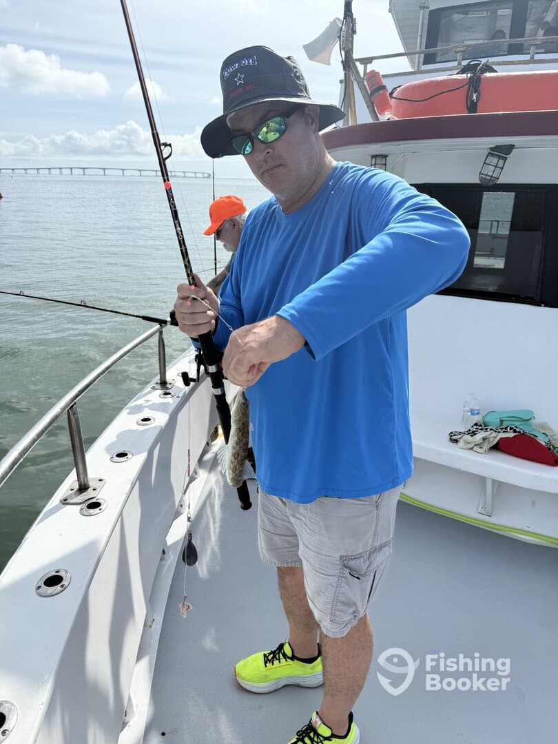 An angler reeling in a fish while fishing on a charter boat, with a bridge visible in the background.