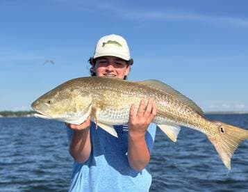 A young angler proudly displaying a large Redfish while fishing on a sunny day.