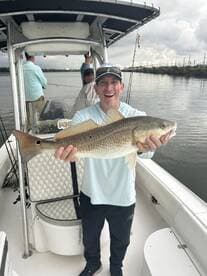 Angler proudly displaying a large Redfish while fishing on a boat, showcasing a successful day on the water.
