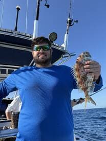 Angler proudly displaying a Snapper while fishing on a boat in open waters.
