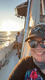 A group enjoying a sunset fishing trip on a boat, with one person taking a selfie while others relax in the background.