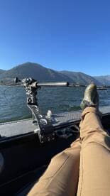 A relaxed angler enjoying the scenic view from the boat, showcasing the interior seating and control area against a backdrop of mountains and clear blue skies.