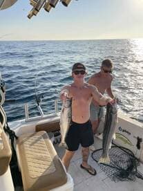 Two anglers proudly displaying their catch of Salmon aboard a boat during a sunny day on the water.