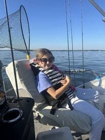 A young girl wearing a life jacket sits comfortably in the boat's seating area, enjoying a calm day on the water.