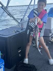 A young girl proudly displays her catch, a catfish, while fishing on a boat, showcasing a fun family fishing experience.