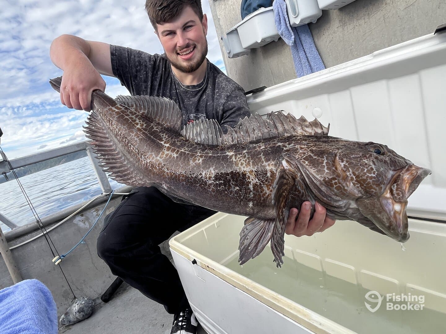 A proud angler displaying a large Lingcod aboard a fishing boat, showcasing the excitement of a successful catch on the water.