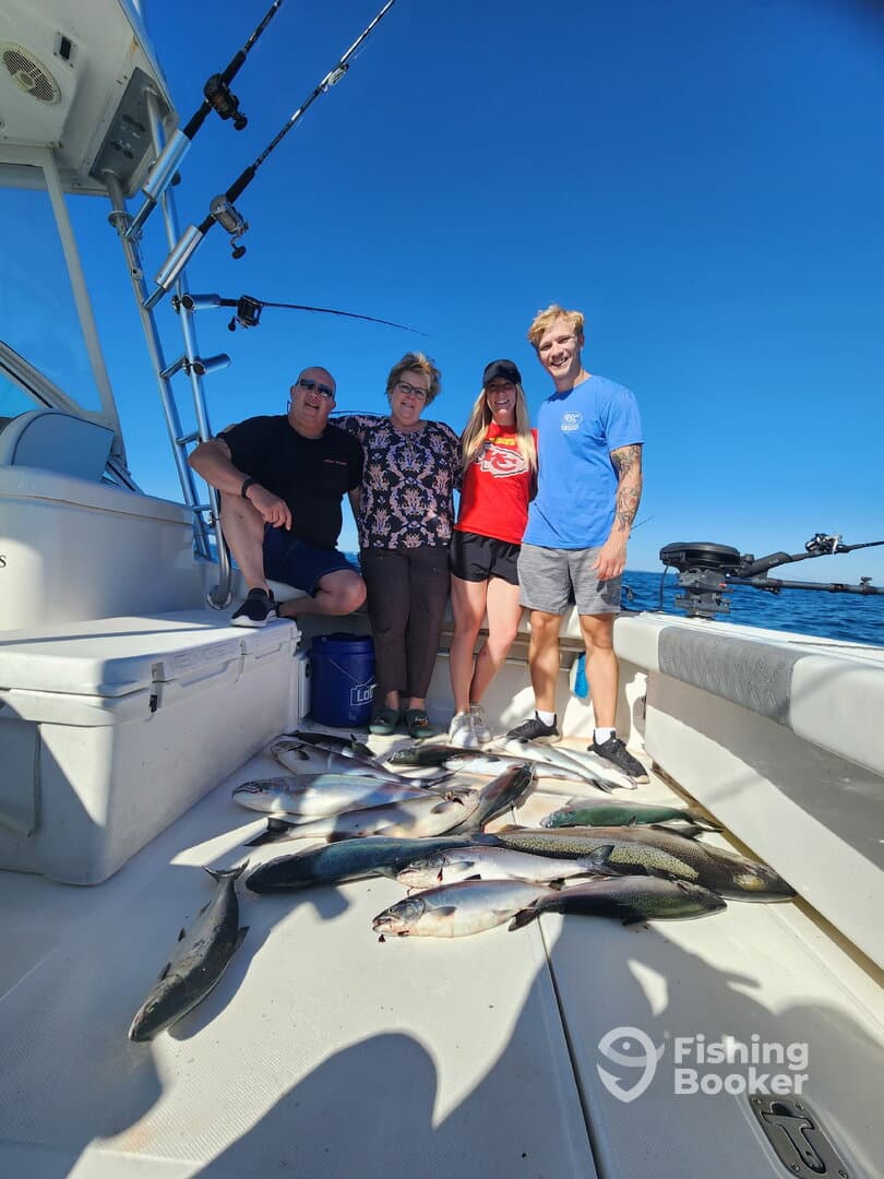 A group of four anglers posing on a boat with a variety of fish laid out on the deck after a successful fishing trip.
