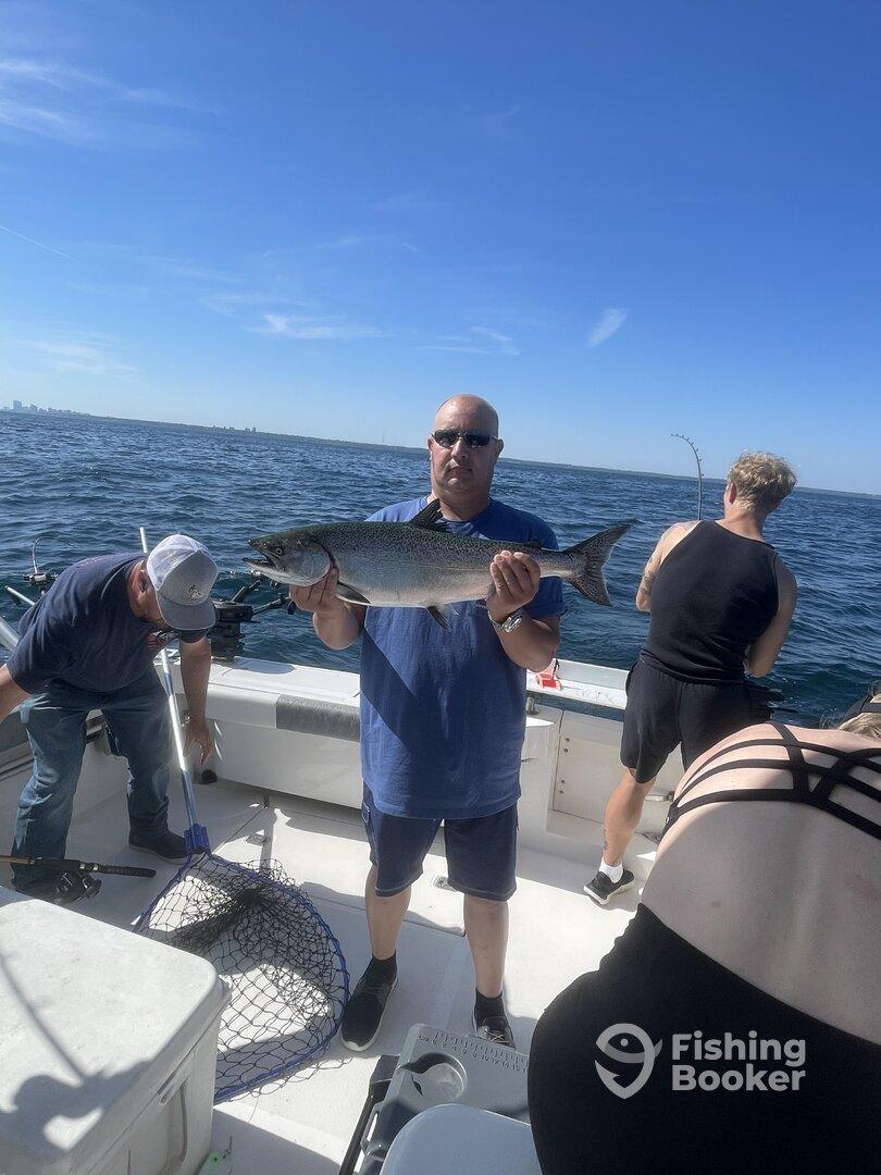 An angler proudly displaying a large fish on a boat during a fishing trip, with a clear view of the open water and other fishermen in the background.