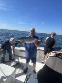 An angler proudly displaying a large fish on a boat during a fishing trip, with a clear view of the open water and other fishermen in the background.