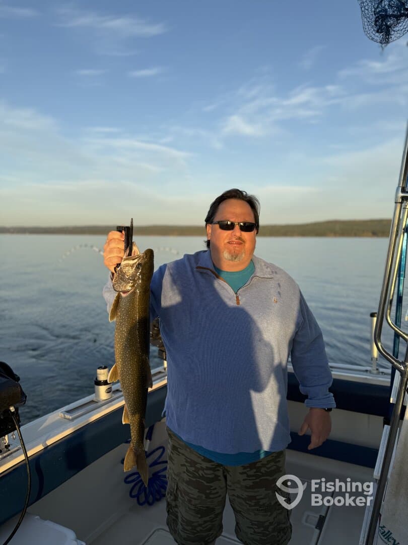 An angler proudly displaying a Lake Trout while fishing on a calm lake, showcasing a successful day on the water.