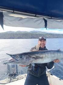 Angler proudly displaying a large Wahoo while fishing off the coast, with scenic cliffs in the background.
