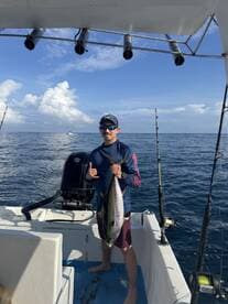 Angler displaying a large Tuna while aboard a fishing boat in open waters, showcasing a successful offshore fishing trip.
