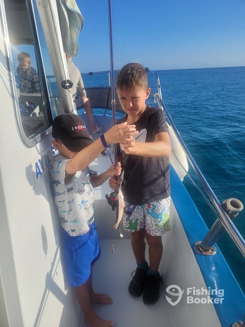 Two young anglers excitedly reeling in a catch while fishing on a boat, showcasing a fun day on the water.
