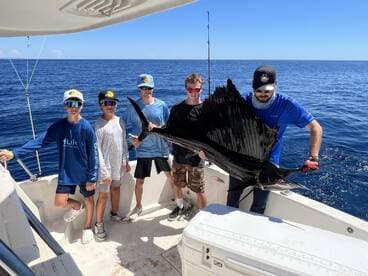 A group of young anglers proudly displaying a large Sailfish aboard a fishing boat in open waters.